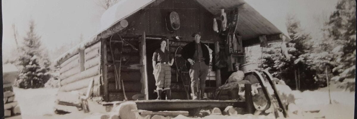 black and white photo of two men standing in front of cabin in winter