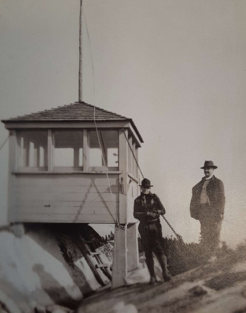 black and white photo of two men standing next to oldest fire lookout station in maine