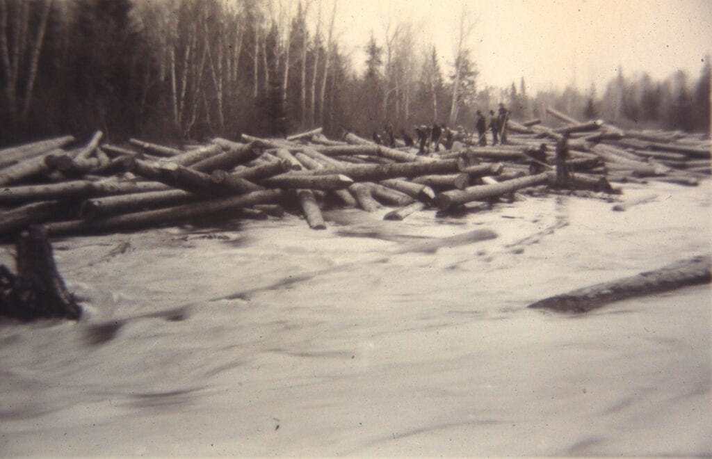 black and white photo of men driving logs down river